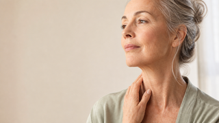 Woman around sixty touching her neck, showing crepey neck skin below the jaw