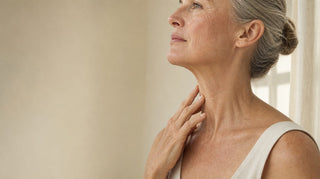 Woman around sixty touching the front of her neck, showing loose crepey turkey neck skin below the jaw