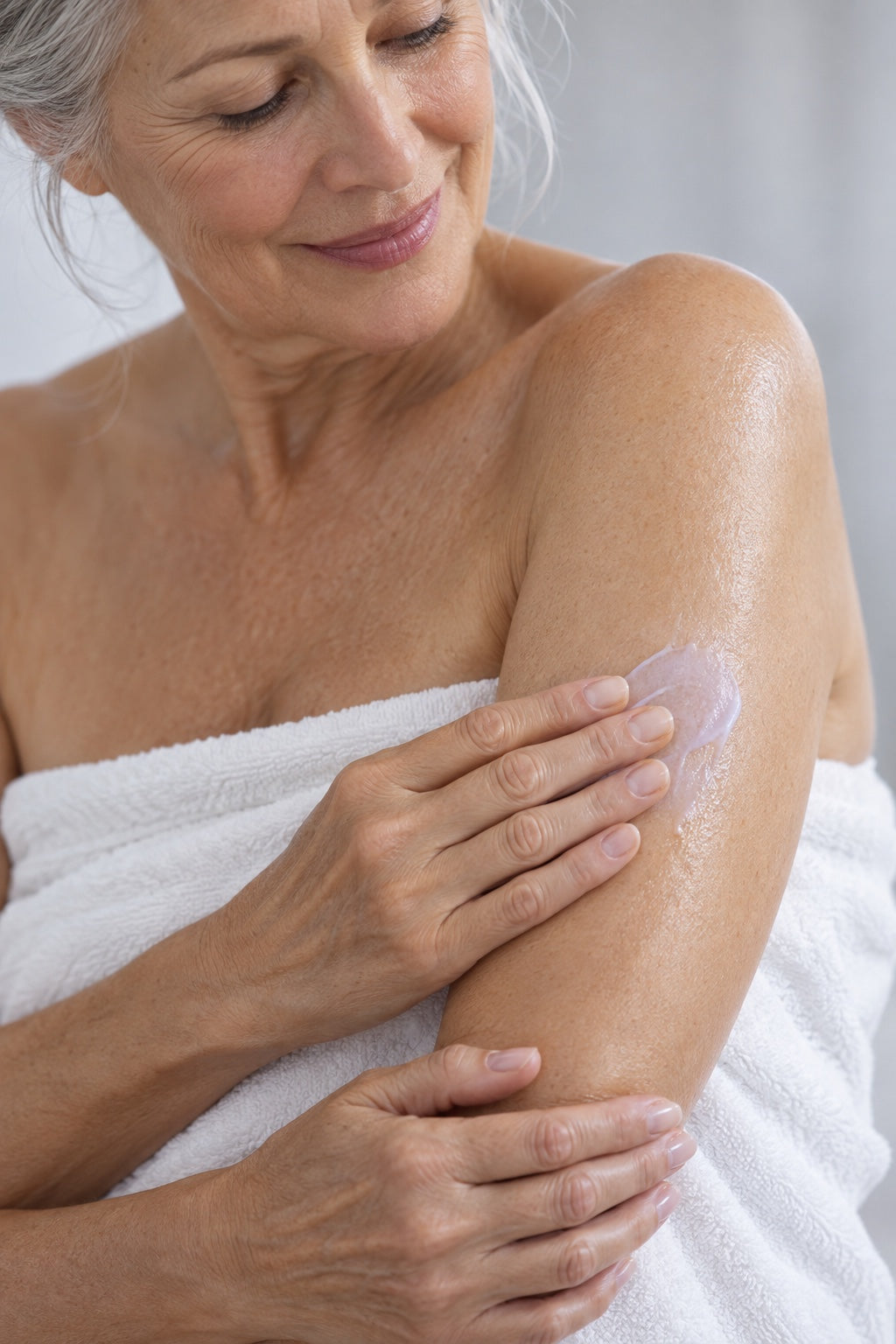 A woman in a bath towel smoothing lotion onto her upper arm